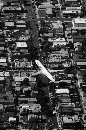 a black and white photo of an airplane flying over a city