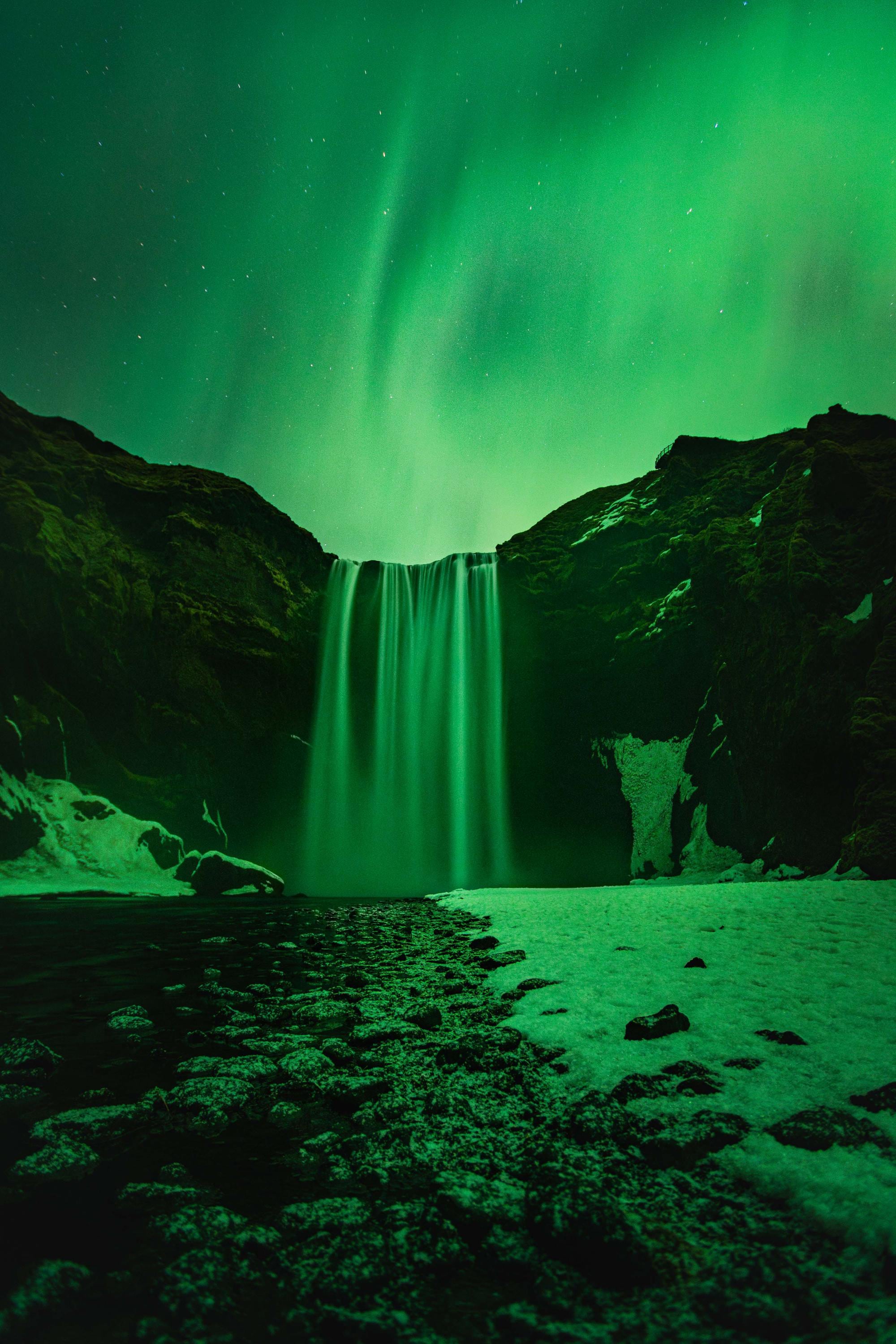 a waterfall with a green light in the sky