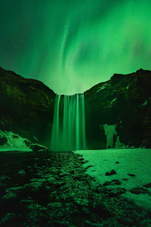 a waterfall with a green light in the sky