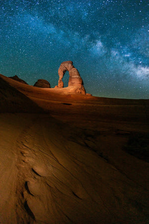 a rock formation in the middle of a desert under a night sky filled with stars