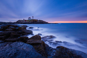 a long exposure photo of a lighthouse on a rocky shore